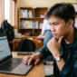 Ilustrasi seorang siswa yang sedang menatap layar laptop dengan ekspresi fokus. Gemini AI