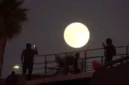 Seorang pria merekam gambar bulan purnama saat terbit di dekat tembok perbatasan yang memisahkan Meksiko dan Amerika Serikat, Senin, 6 Oktober 2025, di Tijuana, Meksiko. (Sumber: Foto AP/Gregory Bull)