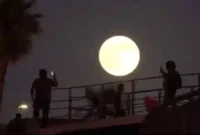 Seorang pria merekam gambar bulan purnama saat terbit di dekat tembok perbatasan yang memisahkan Meksiko dan Amerika Serikat, Senin, 6 Oktober 2025, di Tijuana, Meksiko. (Sumber: Foto AP/Gregory Bull)