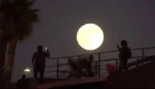 Seorang pria merekam gambar bulan purnama saat terbit di dekat tembok perbatasan yang memisahkan Meksiko dan Amerika Serikat, Senin, 6 Oktober 2025, di Tijuana, Meksiko. (Sumber: Foto AP/Gregory Bull)